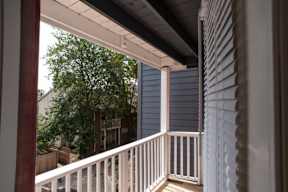a porch with a white railing and a tree in the background