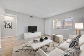 Apartments in Colton, CA - Ardella at Reche Canyon - Modern Living Room with Grey Walls, White Furniture, Large Windows, and Wood-Style Flooring