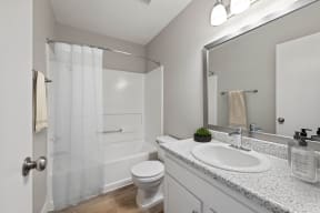 Apartments in Colton, CA For Rent - Ardella at Reche Canyon - Bathroom with Grey Walls and Wood-style Flooring, a Shower and Bathtub Combo, White Toilet and Sink, Spacious Speckled Countertop, and Lar