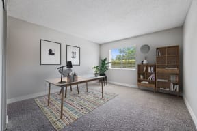 Apartments In Colton, CA - Ardella At Reche Canyon - Home Office With Carpet Flooring, Spacious Desk With Lamp, Chair, Potted Plants, Bookshelves, And Window With Blinds.