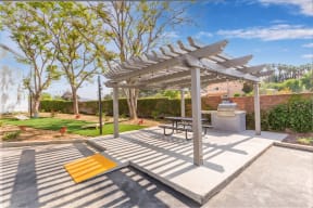 One-Bedroom Apartments In Colton, CA - Ardella At Reche Canyon - Picnic Area Under Pergola With Wheelchair Ramp, BBQ Grill, Table With Benches, Beside Cornhole Area.