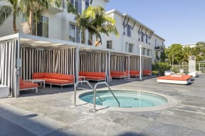 Apartments for Rent in North Hollywood CA - Lofts at NoHo Commons - Round Jacuzzi with Poolside Cabanas, with Palm Trees and Surrounding Greenery, and Side of Building Exterior in Background