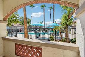 A view from a window looking out at a pool surrounded by palm trees.