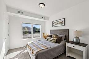 A bedroom with a bed, nightstand, and a window with a view of trees.