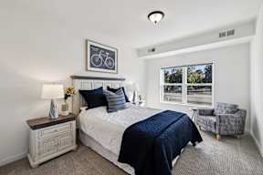 A bedroom with a bed, nightstand, and chair.