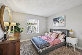 One-Bedroom Apartments in Glendale, AZ - Ardella on 67th - Bedroom with a Large Bed Flanked by Two-Drawer Nightstands Topped with Lamps, and a Wood Dresser with Mirror.