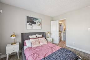 A bedroom with a bed, nightstand, and a painting on the wall.
