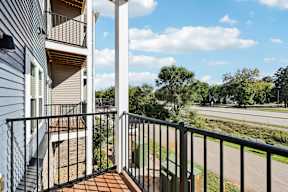 A balcony with a metal railing and a view of a road and trees.