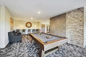 A pool table is in the middle of a room with a stone wall.
