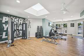 A gym with a variety of equipment including a squat rack, a leg press machine, and a rowing machine.