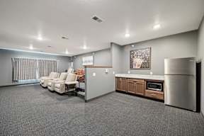 A spacious living room with a grey carpet and a stainless steel refrigerator.