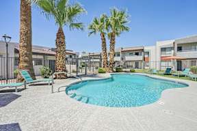 A pool surrounded by palm trees and lounge chairs.
