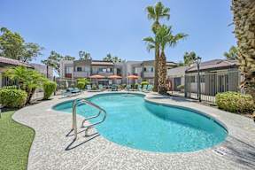 Apartments for Rent in Glendale, AZ - Ardella on 67th - Swimming Pool Featuring Lounge Chairs, Umbrellas, Palm Trees, and Fence.