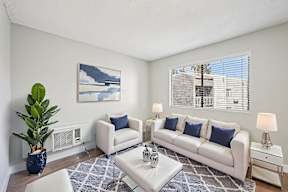 A living room with a white couch, a blue vase, and a painting on the wall.