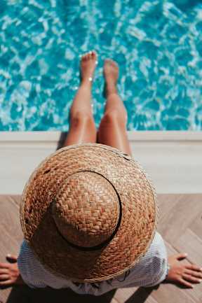 A person wearing a straw hat is sitting by a pool.