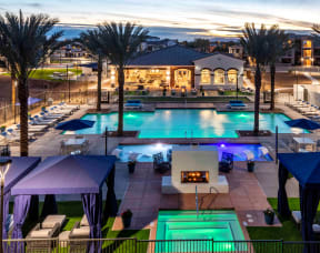 Three Bedroom Apartments in Chandler AZ - The Core Chandler - Resort-Style Pool Area with Lounge Chairs, Spa, Cabanas, Shallow Separate Pool with Submerged Chairs, Turf Areas, and Palm Trees, Shot at Dusk