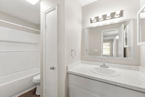 A white bathroom with a sink, mirror, and toilet.
