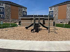 A playground with a slide and swings in front of a building.