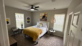 A bedroom with a bed, chair, and a ceiling fan.