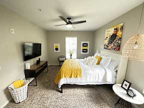 A bedroom with a bed, a TV, a chair, a table, and a ceiling fan.