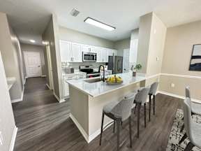 A kitchen with a white island and grey chairs.