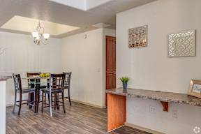 A dining room with a table set for two and a potted plant on the counter.