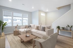 Pet-Friendly Apartments in Vancouver, WA - The Farmstead - Living Room with Sectional, Chair, Coffee Table, Area Rug, Windows, and Staircase.