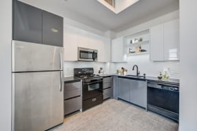 Lofts in North Hollywood CA - Lofts at NoHo Commons - Bright Kitchen with Stainless Steel and Black Appliances, White and Grey Cabinetry, Storage Space, Grey Countertops, and Textured Backsplash