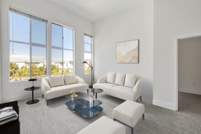 Pet Friendly Apartments in North Hollywood CA - Lofts at NoHo Commons - Living Room with High Ceilings, Couches, Ottomans, Large Windows, Coffeetable, Wall Art, White Walls, Lights, and Side Table