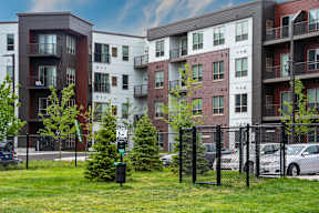 A row of modern apartment buildings with trees and cars parked in front.