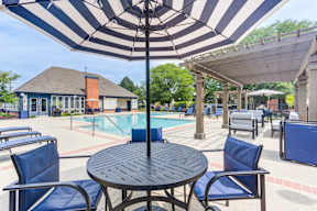 A black and white striped umbrella shades a table and chairs by a pool.