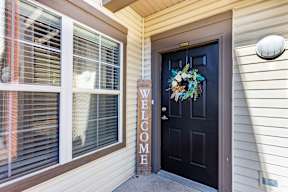 A black door with a wreath and a sign that says "Welcome".