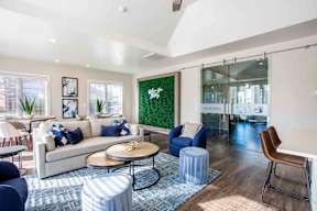 A living room with a white couch, blue ottoman, and a green wall.