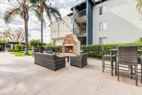Apartments Near The Village at Westfield Topanga - Waterstone - Outdoor Lounge Area with Stone Fireplace, Comfortable Seating, Tables, and Lush Landscaping