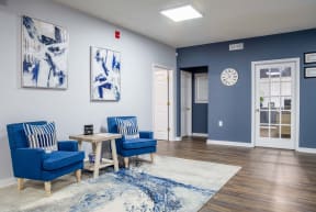 a living room with blue chairs and a table and a clock on the wall
