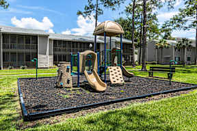 A playground with a slide, swings, and a treehouse in front of a building.