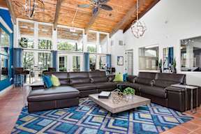 A living room with a brown leather couch and a blue rug.