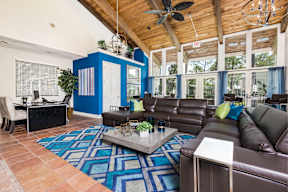 A living room with a brown leather couch and a blue and white rug.