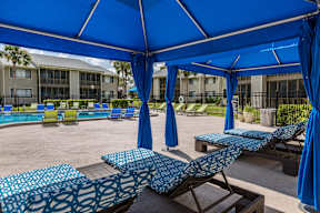 A blue canopy provides shade for a row of lounge chairs.