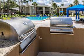 A BBQ grill is on a concrete surface next to a swimming pool.