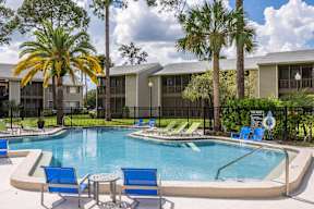 A swimming pool surrounded by blue chairs and palm trees.