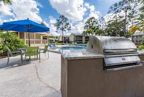 A hot tub sits in the middle of a patio with a grill on the right.