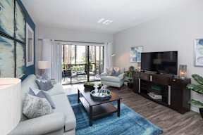 A living room with a grey couch, a coffee table, a television, and a large window.