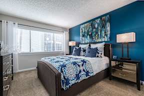 A bedroom with a bed, nightstand, and a window with blinds.