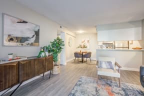 Two-Bedroom Apartments in Glendale, AZ - Ardella on 67th - Living Room with Gray Walls and Wood-Plank Flooring, Sofa, Armchair, Console Table, Windows with Blinds, and Large Area Rug.