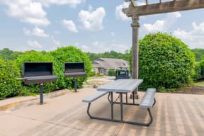 two grills and a picnic table in a park with benches