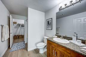 A bathroom with a toilet, sink, mirror, and a doorway leading to another room.