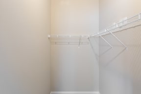 an empty walk in closet with white shelves and a white wall with a wire rack