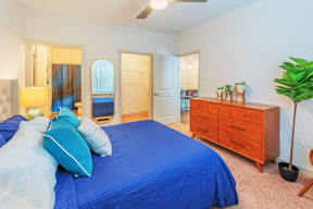 A bedroom with a blue bedspread and a wooden dresser.