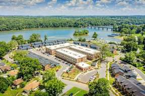 A large building complex is situated in a green area with a river and a bridge in the background.
